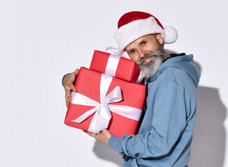 Winter fashion and sales. Smiling senior bearded man holding a pile of gift boxes which he hugs to himself on a white background and looking at the camera with a smile. New year holidays concept.