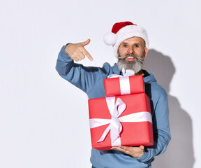 Winter fashion and sales. Smiling senior bearded man points his finger at the gift boxes he holds on a white background and looks at the camera with a smile. Concept of the New Year holidays.