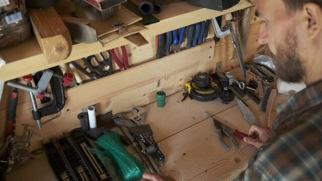 Top view bearded man joiner woodworker choosing construction carpentry tools in his workshop. DIY concept.