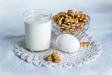 On a white napkin, a glass of milk, an egg, cookies in a plate. On a white or light background.
selective focus. Space for text, banner