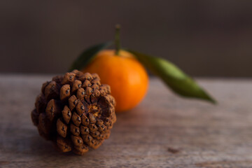 pine cone and fresh unfocused mandarin with leaves on wooden weathered garden table close up, fresh and organic food, christmas taste