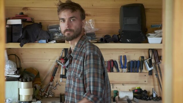 Portrait of brutal worker man stands in workshop, construction carpentry tools in the background. Cheerful craftsman. DIY concept.