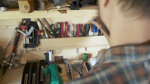Rear view joiner woodworker organizing construction carpentry tools in his workshop. DIY concept.