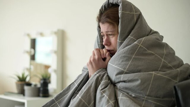 A woman is freezing and wrapped in a blanket in bed to keep warm. Turning off heating and a sudden arrival of cold weather, the onset of winter