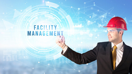 Handsome businessman with helmet drawing FACILITY MANAGEMENT inscription, contruction business concept