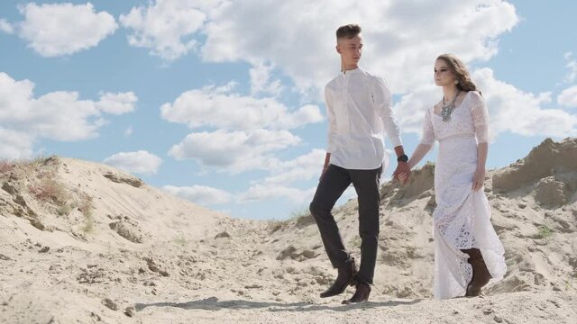 Stylish beautiful couple walking on a sandy quarry, against a blue sky, boho wedding concept
