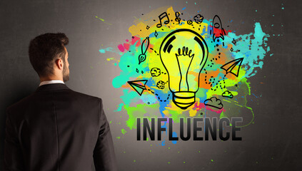 businessman drawing colorful light bulb with INFLUENCE inscription on textured concrete wall, new business idea concept