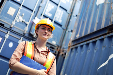 Young woman engineers standing in the shipping yard tracking the cargo inventory and checking container box for safety.