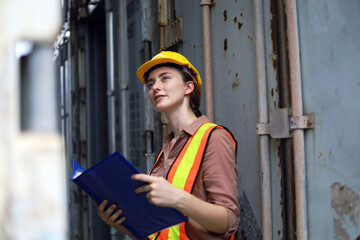 Young woman engineers standing in the shipping yard tracking the cargo inventory and checking container box for safety.