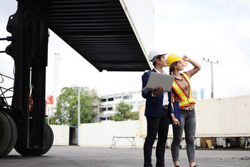 Young Engineers standing in the shipping yard tracking the cargo inventory and checking container...