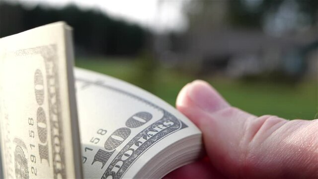 Close-up of a male hand flipping through a stack of 100 dollar bills USD