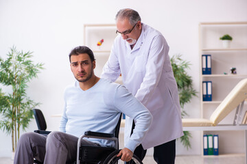 Young man in wheel-chair and old doctor traumatologist
