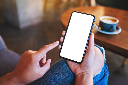 Mockup image of a woman holding and pointing finger at mobile phone with blank white desktop screen in cafe