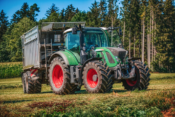 Green tractor with a loading wagon at a meadow