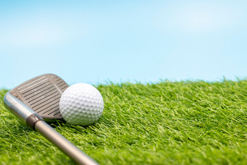 Golf ball with iron are on green grass on blue sky background