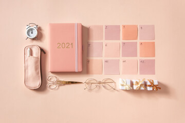 Flat lay of notepad with words Goals 2021, colorful sticky notes, o'clock, pen and pen case. Coral pink background