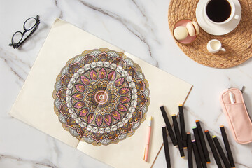 Woman drawing and coloring mandala in sketchbooks with colorful markers while having a breakfast