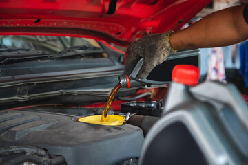 Car mechanic working in the local garage by pouring new oil into the engine. Oil change of car maintenance services.