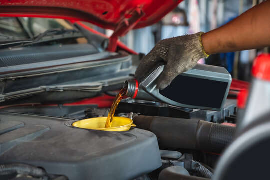 Car mechanic working in the local garage by pouring new oil into the engine. Oil change of car maintenance services.