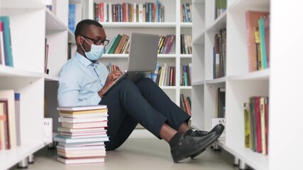 University library: african american man in a mask during quarantine covid-19 prepares for the exam, the concept of a student being education.