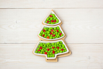 Christmas sweets. Candy in a plate in the shape of a Christmas tree on a wooden background. Place for your text. View from above. Candy bar.