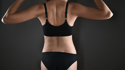 Caucasiana woman showing her biceps muscles on the arms in black sport underwear over gray...