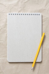  Gray notepad with white coiled spring and pencil on a background of beige crumpled craft paper