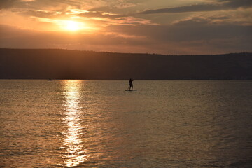 Man sail on a SUP board in a large lake during sunrise. Stand up paddle boarding - active recreation in nature. The Sea of Galilee, Lake Tiberias, Kinneret, Kinnereth. High quality photo.