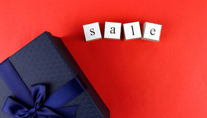 The inscription on a red background "SALE" from wooden cubes with a blue gift box. Black Friday, Christmas, discounts and online shopping