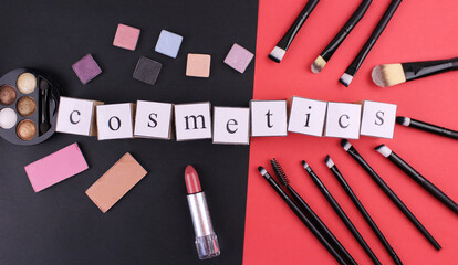 The inscription "cosmetics" from wooden cubes on a red-black background with cosmetics. Various cosmetics on a red and black background. Makeup brushes with cosmetic products
