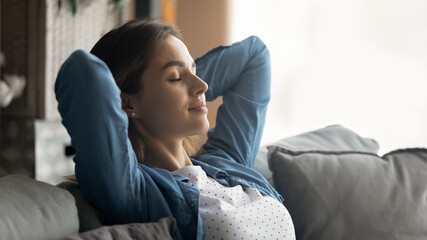 Wide banner panoramic view of happy young Caucasian woman sit rest on couch sleep or take nap. Calm millennial female relax on sofa in living room, breathe fresh air, relieve negative emotions.