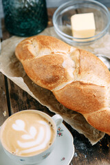 Fresh bread and butter on a wooden background. A Cup of cappuccino on a saucer.