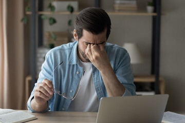 Unwell young man overwhelmed with computer job take off glasses have blurry vision or dizziness....