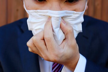 スーツを着て、マスクを日本人男性が鼻を塞いでいる