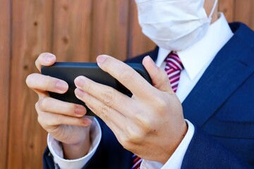 スーツとマスクを着用したアジアの男性がスマートフォンを見ている
