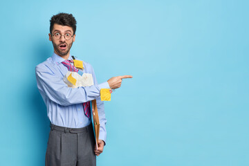 Horizontal shot of surprised intelligent male student surrounded with papers dressed in formal...