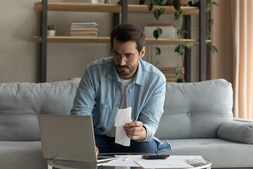 Concentrated millennial man look at laptop paying bills or taxes online on gadget. Focused young Caucasian male manage household finances expenditures, take care of family budget using computer.