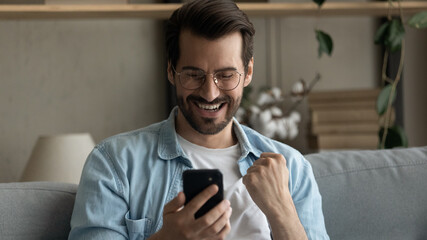 Obraz na płótnie Canvas Wide banner panoramic view of excited young Caucasian man look at smartphone screen celebrate online win or victory. Happy millennial male triumph feel excited with good news on cellphone gadget.