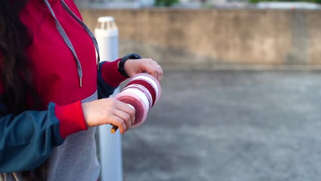 slow motion shot of girl lady woman using both hands to wind string on a charkhi spool for kite flying with different colors for the saddi plain thread and red for the glass covered manjha for kite