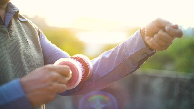 Man holding a charki phirki thread spool in the crook of his elbow and winding it with the other hand to ensure taughtness for the famed kite fighting festival of makar sankranti uttarayana