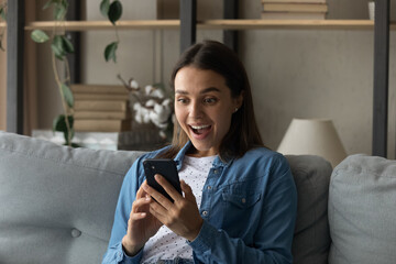 Amazed happy young Caucasian woman look at cellphone screen shocked by unexpected good sale offer...