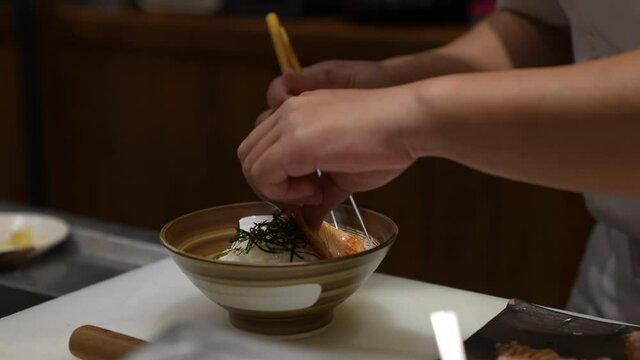 4K Close up hand of Professional chef decorate burned slice salmon rice bowl on kitchen counter. Male chef preparing delicious healthy food fish menu aburi salmon ikura donburi in japanese restaurant