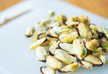Selective focus closeup photo fresh and raw mussels or clams shelled seafood piled on a plate or white plastic cutting board prepared for cooking use as a background image.