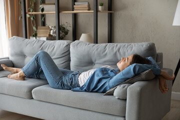 Exhausted young Caucasian woman lying relaxing on sofa in living room sleep or take nap at home....