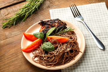 Plate of soba with chicken, tomatoes and spinach on a linen napkin next to a fork and a sprig of rosemary.