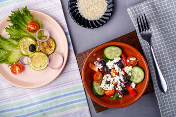 plate with grilled zucchini on lettuce leaves and greek salad on a gray background on a napkin with a fork