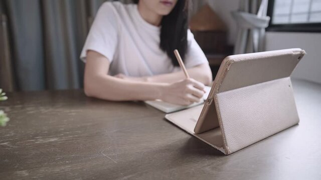 Young asian woman study online by watching tablet, home school tuition, stay at home concept, self discipline on education, hand writing down on notebook, taking lecture from online class course