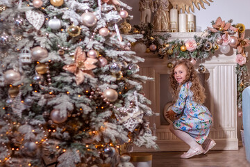 A beautiful laughing girl with curly long hair stands near a decorated Christmas tree. Decorates the Christmas tree.