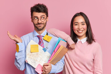Puzzled male entrepreneur shrugs shoulders with hesitation holds folders covered with stickers and...