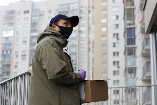 Courier in face mask with a parcel at the entrance of home verifies the information in the documents.